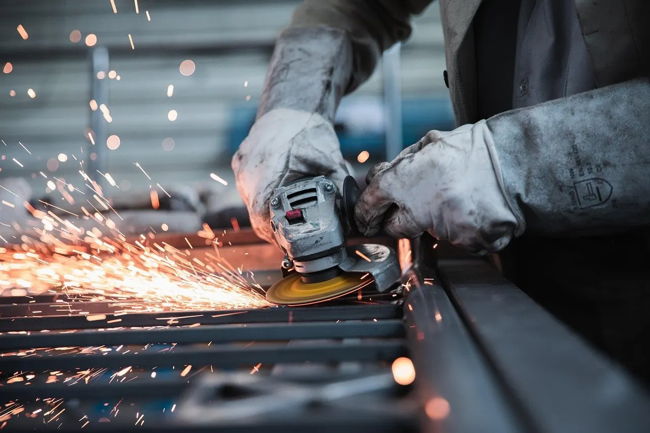 Behandschuhte Hände führen eine Trennscheibe über Metallprofile, dabei sprühen zahlreiche Funken.